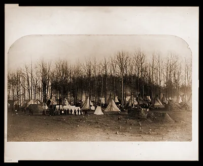 Union Army camp showing large tents errected among trees and soldiers posed by row