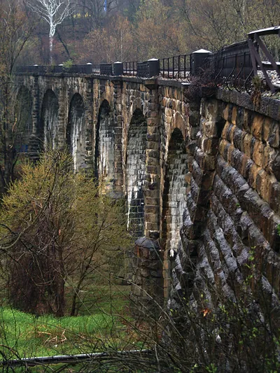Stone arch railway viaduct with iron railings through trees