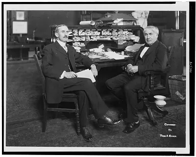 [Thomas Alva Edison, full-length portrait, seated at his desk, facing left, with Mr. Wilson]