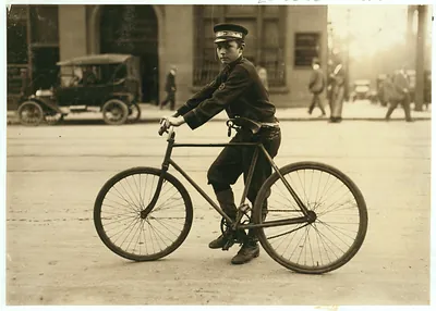 Boy messenger in cap riding a bicycle on city street