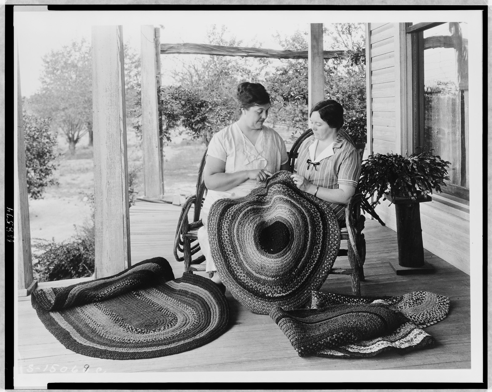 [Two women making rugs on porch], [between 1925 and 1930(?)] — historic photograph