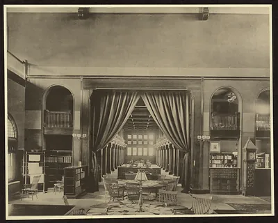 Library reading room with curtains, long tables and bookcases