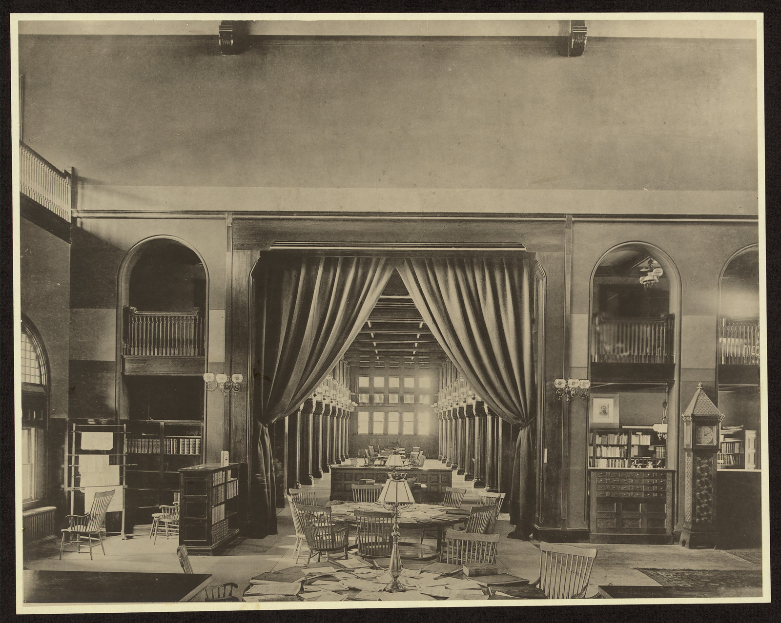 Library reading room with curtains, long tables and bookcases — historic image