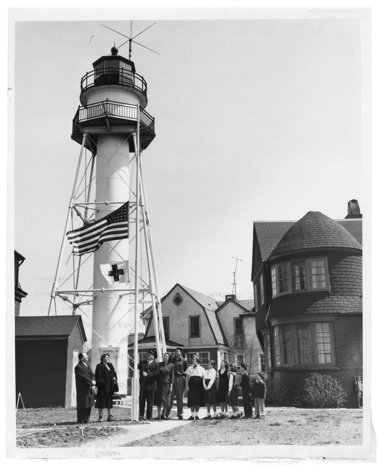 Lighthouse tower with flag and group of people on lawn — historic image