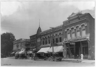 [Commercial block of unidentified town, showing autos parked]