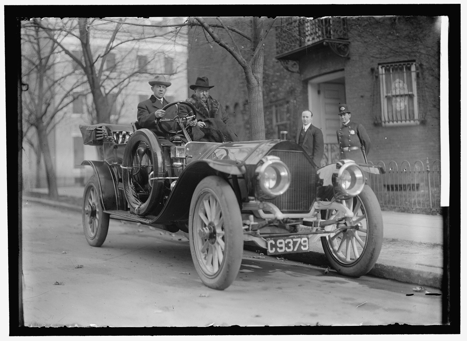 Two men riding in an early automobile, plate C9379 — historic image