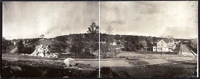 Panoramic black and white view of a hillside road and houses