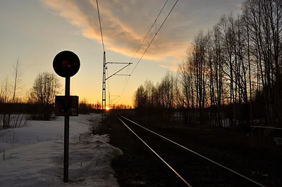 Railroad track at sunset with signal and overhead wires