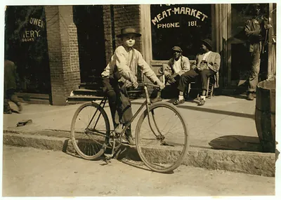 Boy standing beside bicycle in front of meat market