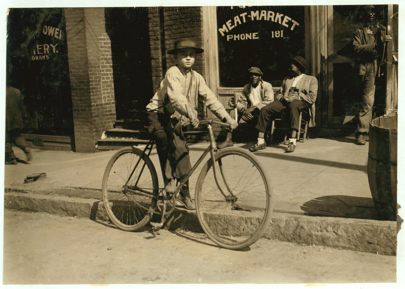 Boy standing beside bicycle in front of meat market — historic image