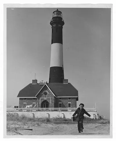 Child running past striped lighthouse and keeper's house