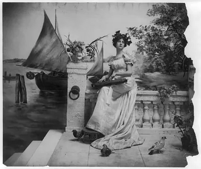 [Young woman modeling: Full lgth., leaves on head, seated on sea-wall holding zither]