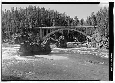 Concrete arch bridge over rapids, pine forest, black and white photograph