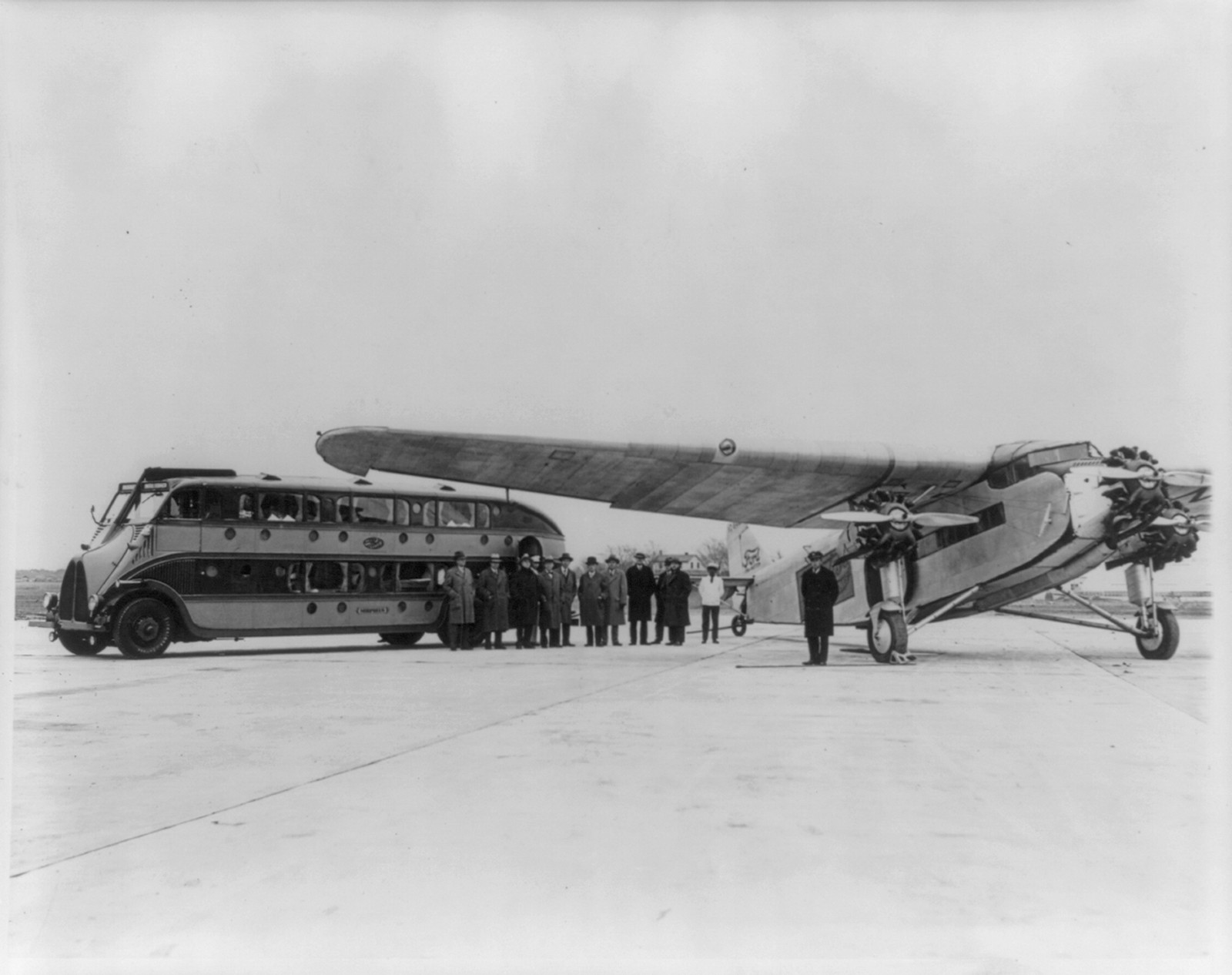 Greyhound bus, world's 1st motor coach sleeper, parked next to Ford Tri-motor transport; 10 named corporate executives stand before bus. Chicago, 1929 Oct. 26. — historic photograph