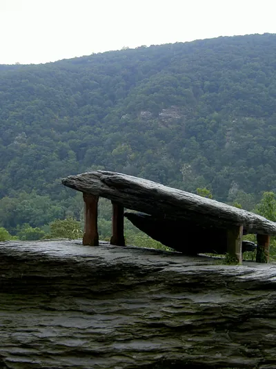 Rustic wooden bench on rock overlooking forested mountains