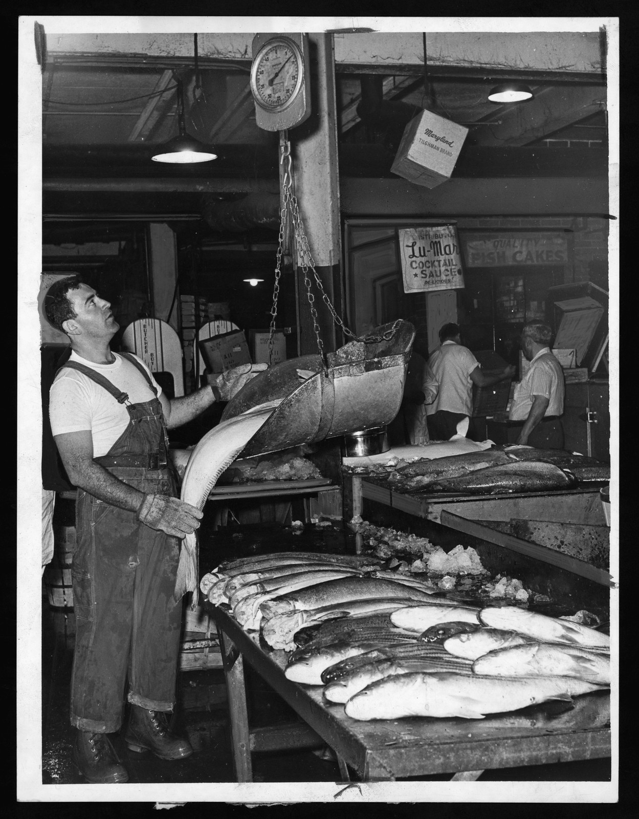 Man weighing fish on a scoop scale at market — historic image