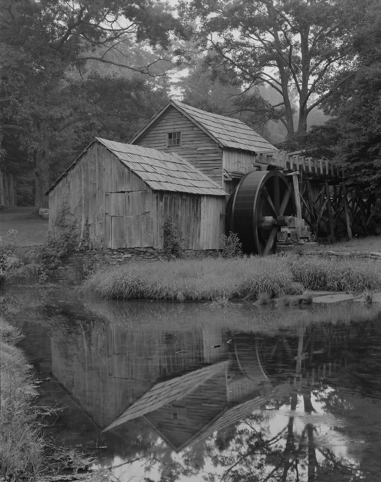 Old wooden mill with waterwheel above a reflecting pond — historic image