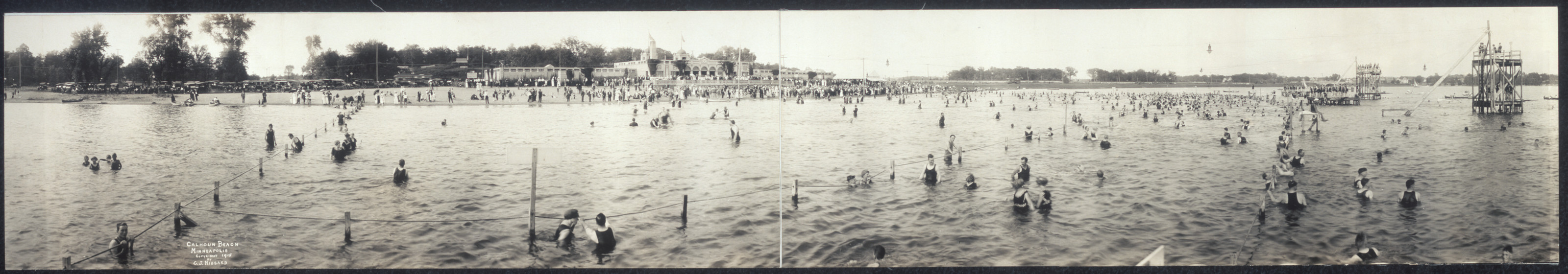 Crowded lakeside beach with swimmers and pavilion, panoramic photograph — historic photograph
