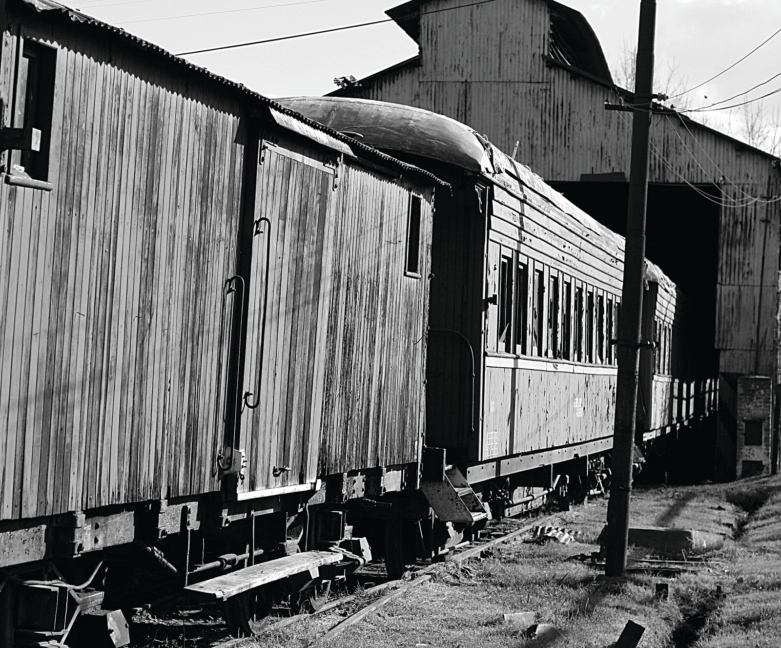 Old passenger rail cars beside a corrugated metal shed — historic image