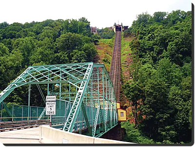 Steep incline railway beside green steel truss bridge