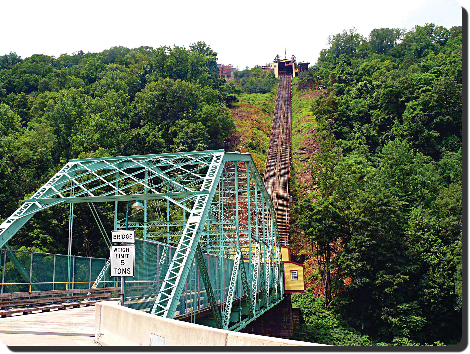 Steep incline railway beside green steel truss bridge — historic image