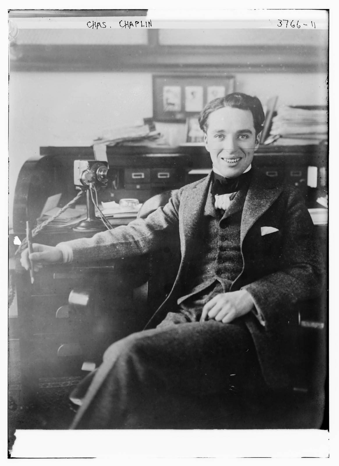 Chas. Chaplin seated at a desk, smiling — historic image