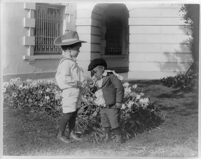 [Quentin Roosevelt as a child in front of a flower garden and Roswell Newcomb Pinckney smelling a flower at the White House, Washington, D.C.]