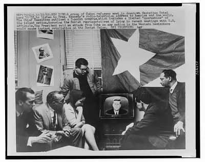 [Group of Cuban refugees gather in a Manhattan Hotel room in front of television as President Kennedy announces a quarantine" of their home island during the Cuban Missile Crisis in 1962]"