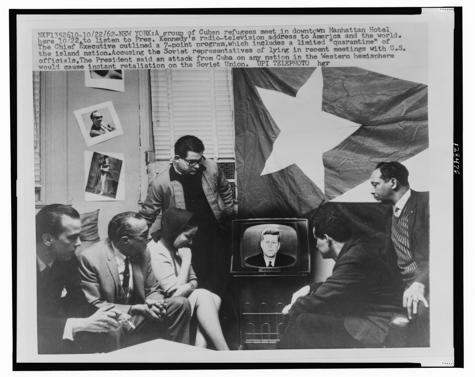 [Group of Cuban refugees gather in a Manhattan Hotel room in front of television as President Kennedy announces a quarantine" of their home island during the Cuban Missile Crisis in 1962]" — historic photograph