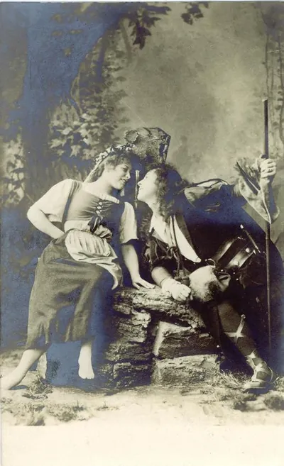Costumed couple posed on rock in studio backdrop, sepia photograph