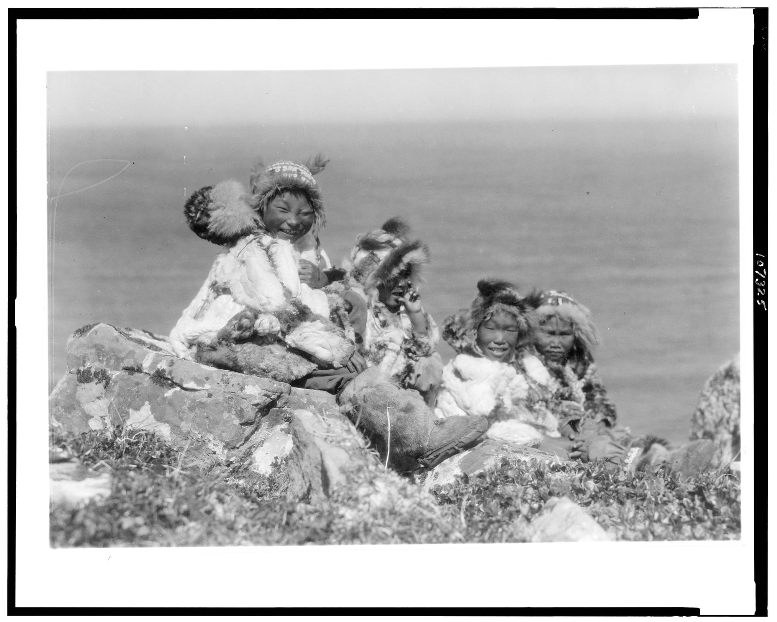 [Four Eskimo children, at edge of cliff, in holiday costume, Nunivak, Alaska], c1929. — historic photograph