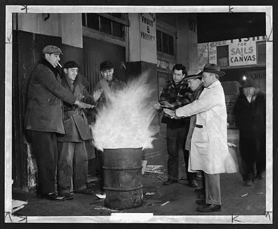 Men warming hands over a fire barrel outside a produce market