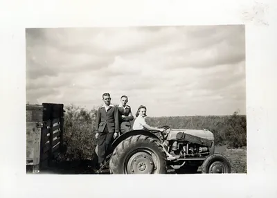 Young woman driving a vintage tractor with two men