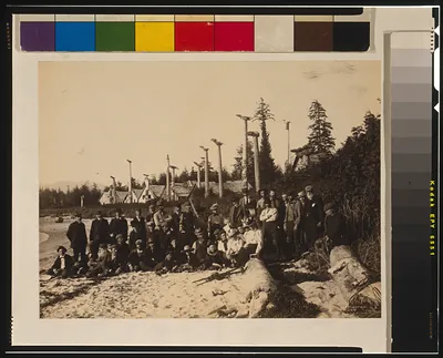 [Harriman Alaska Expedition members pose on beach at deserted Cape Fox village, Alaska, 1899, with Tlinget totem poles in background] / Curtis.