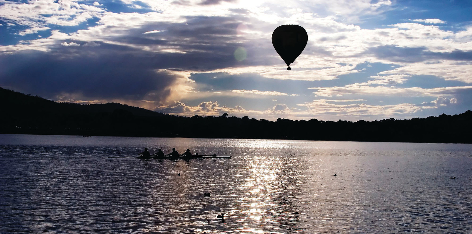 Rowers on a lake beneath a hot air balloon — historic image