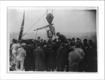 Crowd watching a crane lift an eagle emblem with flags