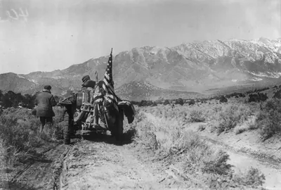 [New York to Paris auto race, 1908: rear view of auto with tire chains and U.S. flag on crude road; high mountains in distance]