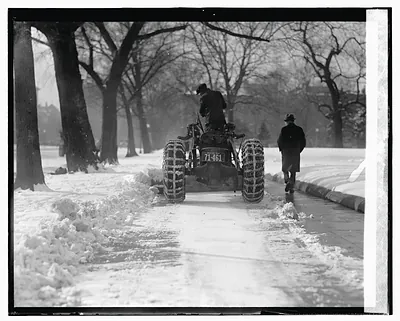 Tractor with snow chains clearing a snowy walkway
