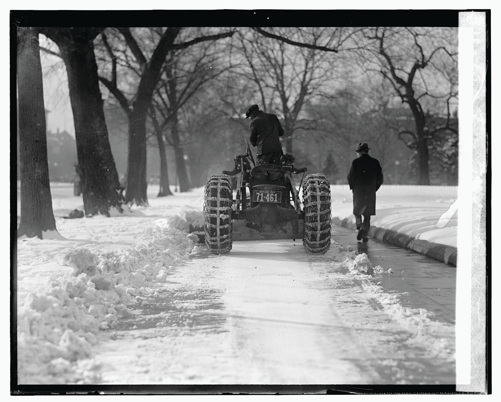 Tractor with snow chains clearing a snowy walkway — historic image