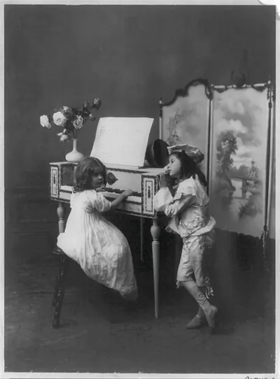 Two children in costume beside a spinet, photograph