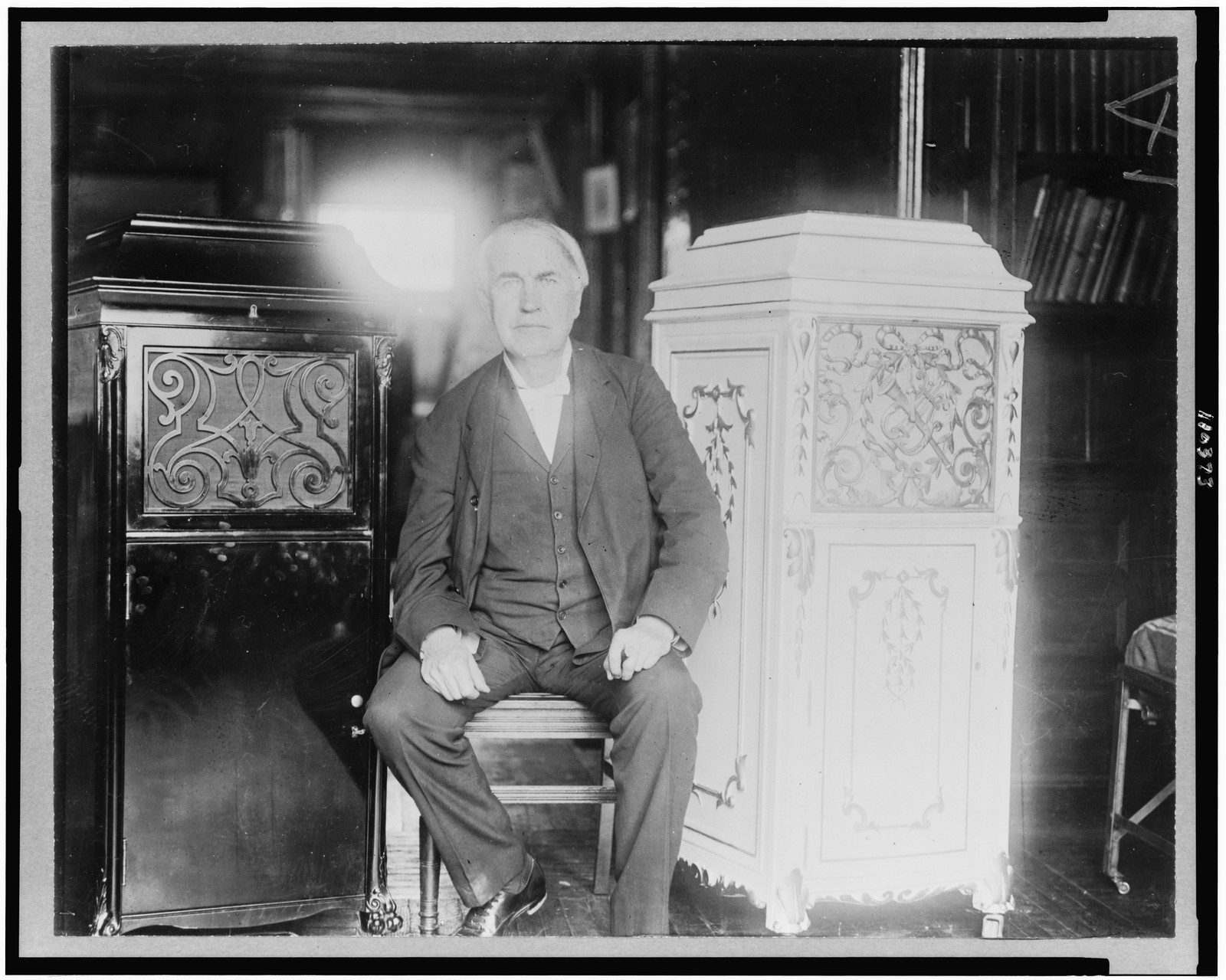 [Thomas Alva Edison, full-length portrait, seated, facing front, between two phonograph cabinets, one of which is made of concrete], c1912. — historic photograph