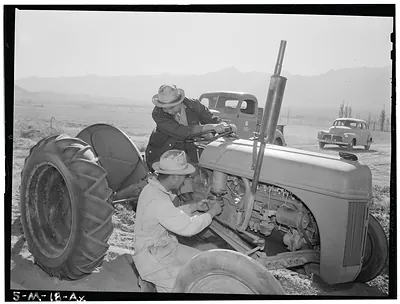Two men repairing a tractor in an open field