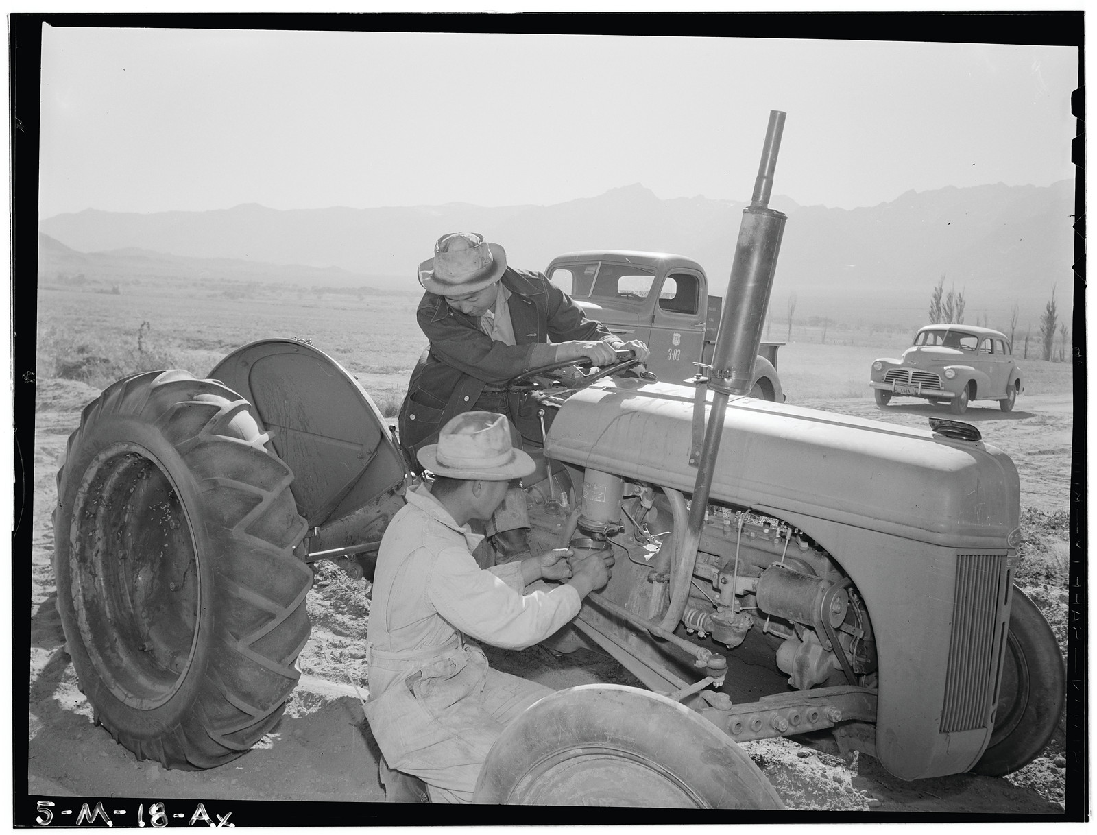Two men repairing a tractor in an open field — historic image