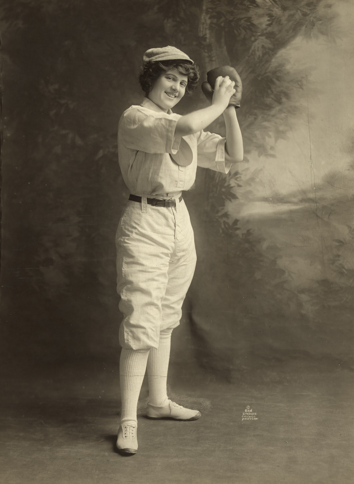 Smiling woman in baseball uniform holding a glove, studio portrait — historic image