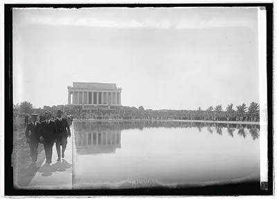 Men walk beside Lincoln Memorial reflecting pool before crowd