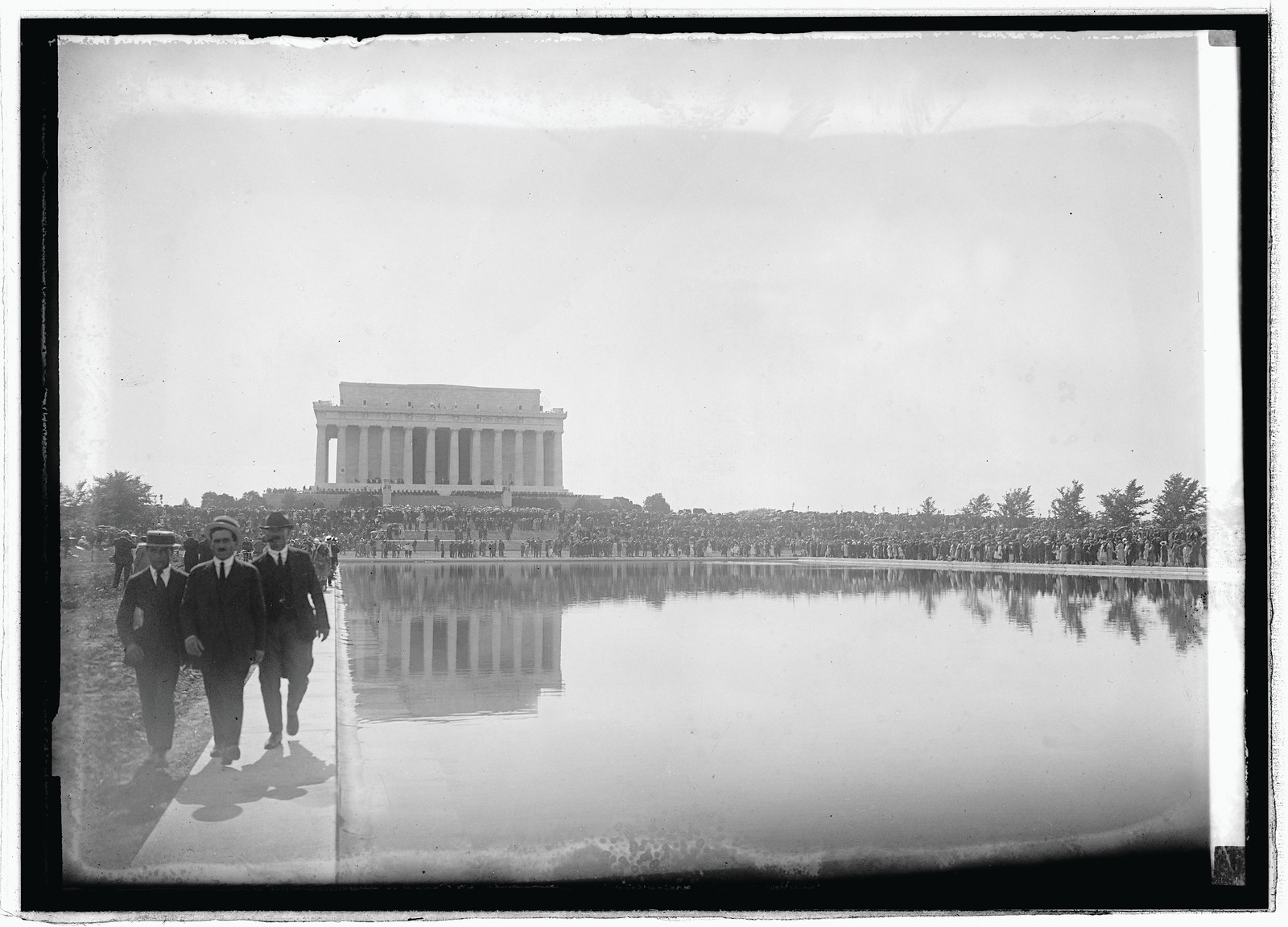 Men walk beside Lincoln Memorial reflecting pool before crowd — historic image