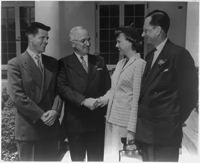 [Harry Truman shaking hands with a woman, standing between two men]