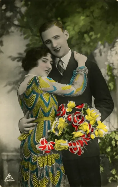 Hand-colored postcard of a couple embracing with a flower bouquet