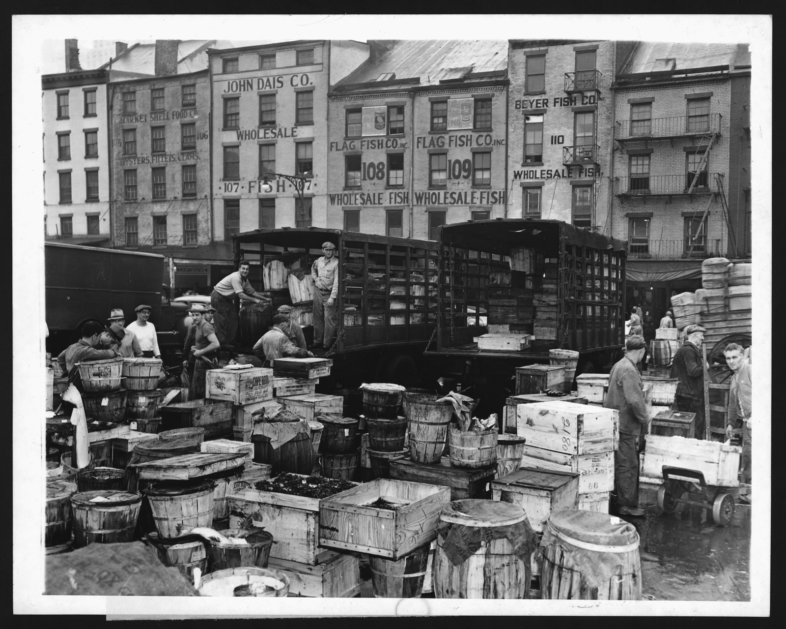 Wholesale fish market with wooden crates, barrels and loading trucks — historic image