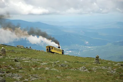 Yellow cog railway train descending a grassy mountainside, steaming